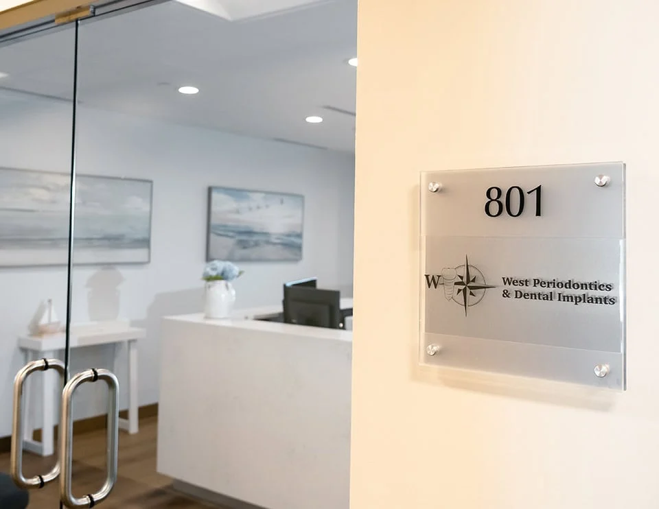 West Periodontics and Dental Implants office entrance with signage displaying "801" and logo, modern reception area featuring white decor and artwork.