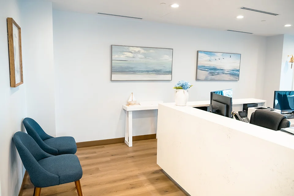 Modern dental office reception area with blue chairs, ocean-themed artwork, and a welcoming front desk, emphasizing patient comfort at West Periodontics and Dental Implants.