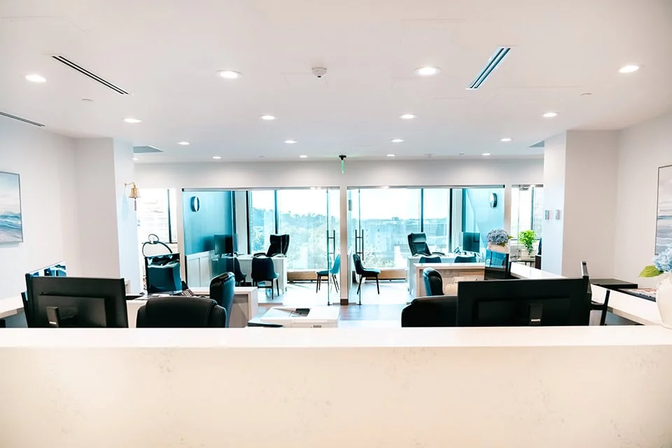 Modern dental office interior with reception area, multiple workstations, and large windows providing natural light, emphasizing patient comfort and advanced dental care at West Periodontics and Dental Implants.
