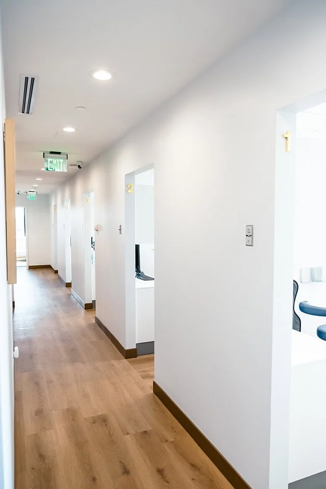Dental clinic hallway with numbered treatment rooms, bright lighting, and wooden flooring, emphasizing a calm and welcoming environment for patients receiving IV sedation during dental procedures.