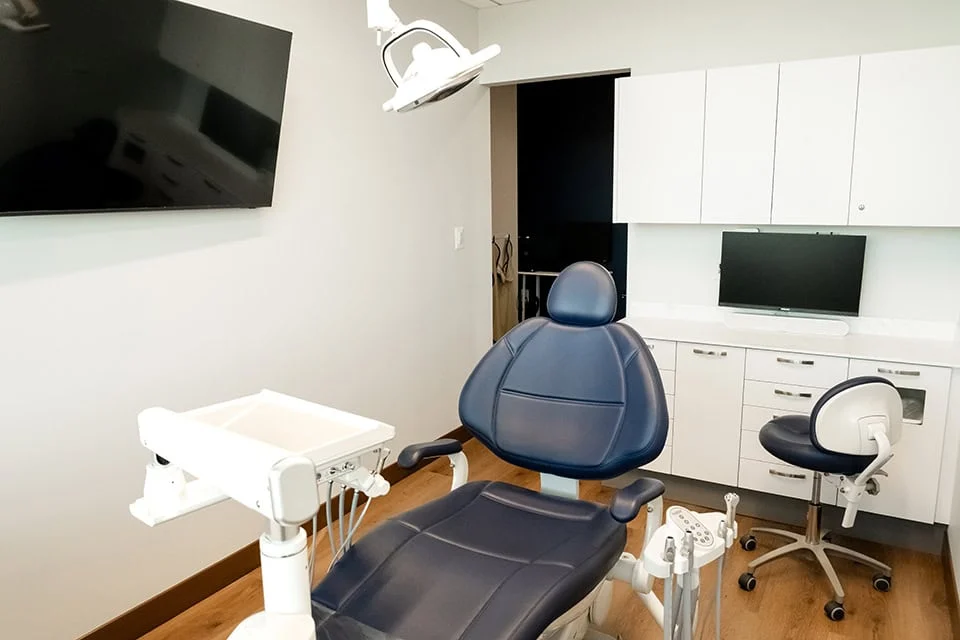 Dental treatment room featuring a comfortable blue dental chair, overhead light, and modern equipment, emphasizing a calming environment for oral sedation procedures at West Periodontics & Dental Implants.